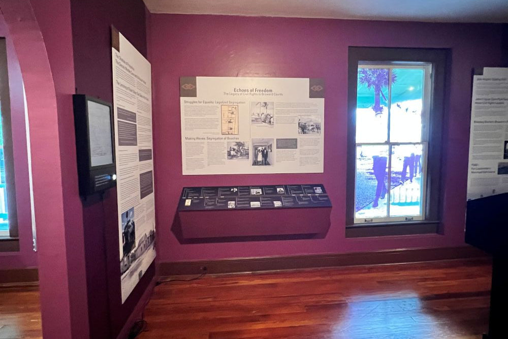 Display case with informational materials on a purple wall in a room with wooden flooring.